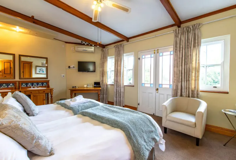 Cozy bedroom at Evergreen Manor and Spa with king bed, white armchair, wooden beams, French doors to garden, and ceiling fan.