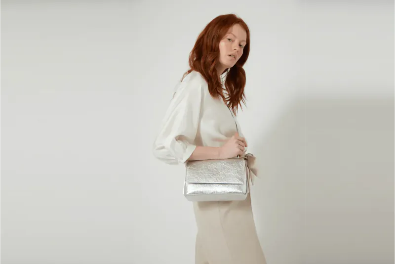 Red-haired woman in white blouse and skirt holding silver Luxtra handbag, side view on white background