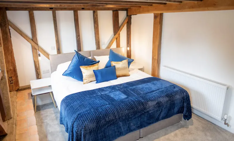 Luxurious king bed with blue pillows and duvet in timber-framed barn room at Chart Hills The Barn