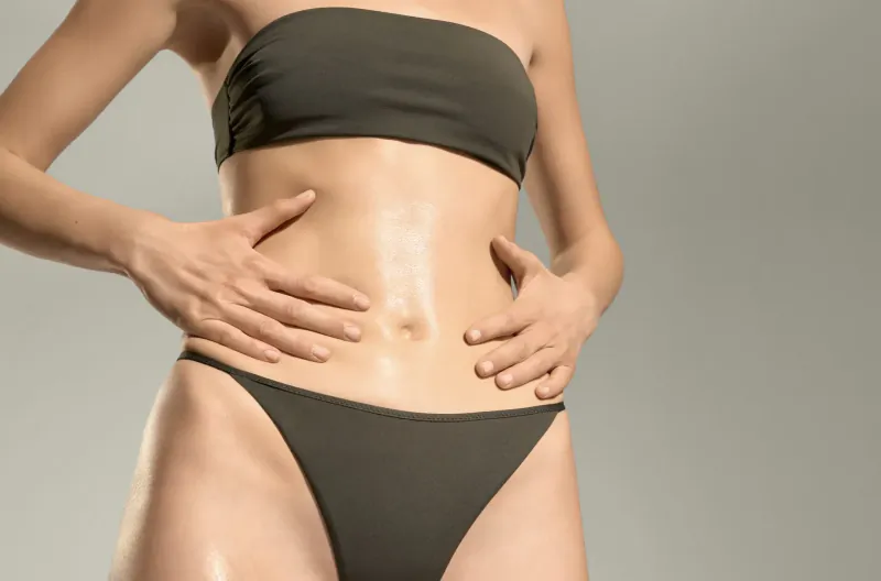 Woman in gray tube top and bottoms holds shiny abdomen, promoting anti-cellulite firming gel
