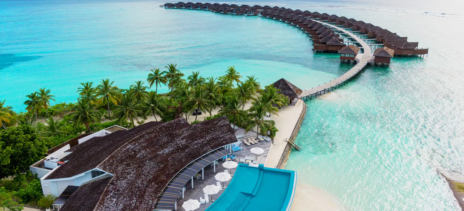 Aerial view of Hideaway Beach Resort & Spa Maldives: overwater villas on turquoise lagoon, thatched buildings, infinity pool, white sand beach, palms.
