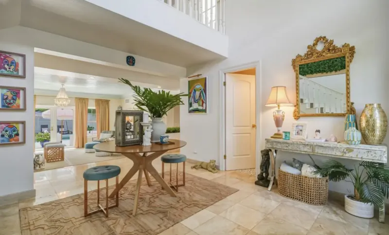 Spacious Lyford Cay entryway with round wood table, stools, plants, art, ornate mirror, and open living area
