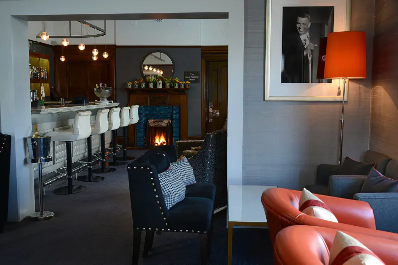 Northcote Hotel lounge with white bar stools, turquoise fireplace, navy armchairs, and black-and-white portrait.