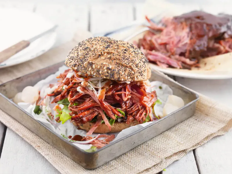 Pulled pork burger with coleslaw on seeded bun in metal tray, side pulled pork on plate
