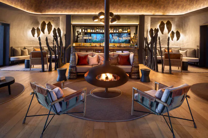 Cozy lounge in Mashatu Euphorbia eco camp with central spherical fireplace, plush sofas, wooden decor, and tribal art.