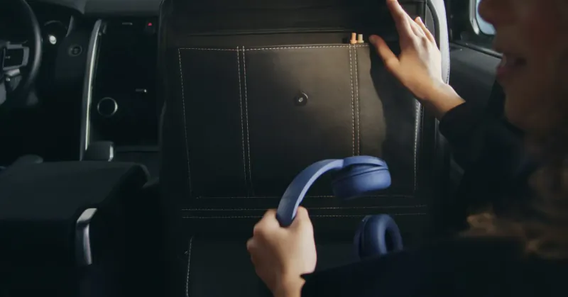 Woman in luxury SUV driver's seat holding blue headphones, hand in leather console compartment