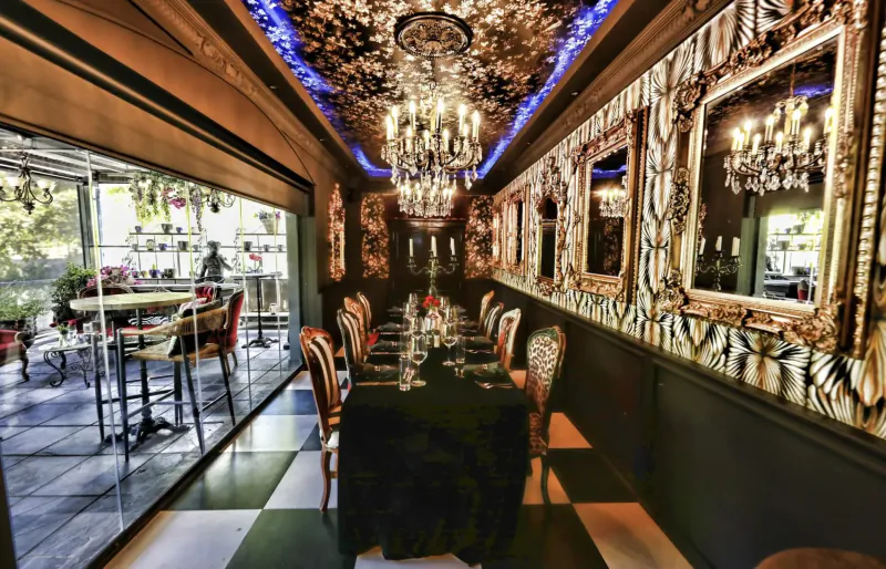 Opulent Simon’s Restaurant interior with ornate gold mirrors, chandeliers, black-draped dining table, and garden patio view.