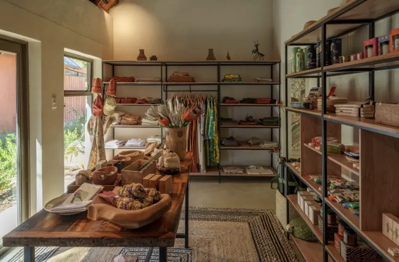 Cozy gallery shop with wooden shelves of pottery, baskets, fabrics, and wooden table displaying bread and bowls.