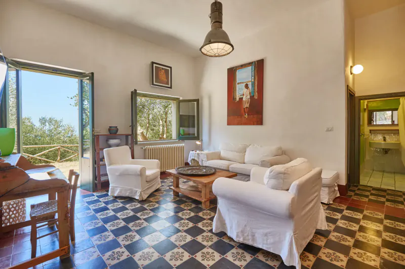 Luxury Sicilian villa living room with white sofas, checkered tile floor, industrial lamp, art, and hill views