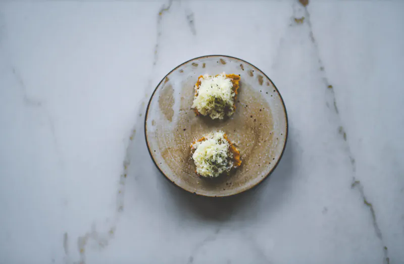 Two pieces of toasted bread topped with white cheese crumbles on a rustic plate on marble surface