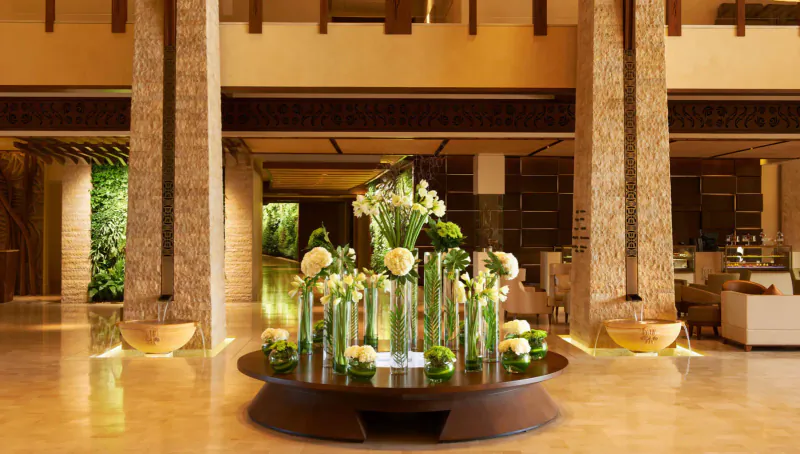 Central floral arrangement of white lilies and greenery on round table in Sofitel Dubai The Palm lobby with stone pillars.