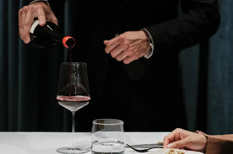 Sommelier pouring red wine from bottle into glass at elegant table in Michelin-starred restaurant