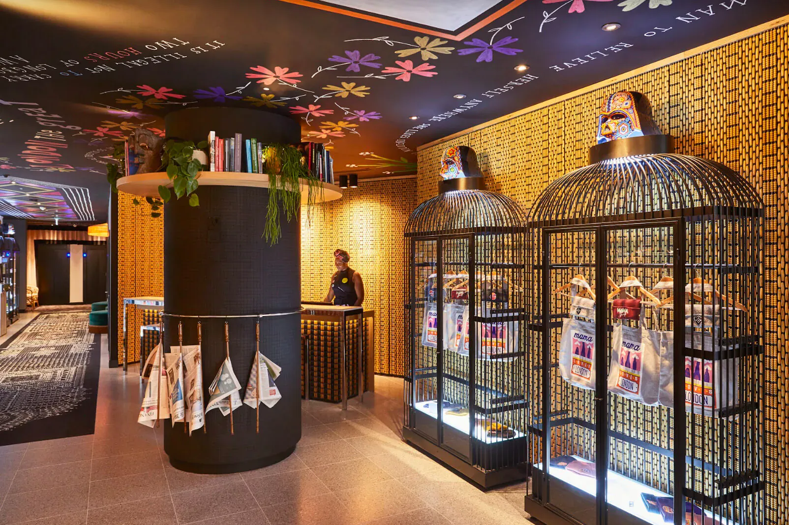 Mama Shelter East London lobby with birdcage decor, floral ceiling, bookshelves, counter, and staff.