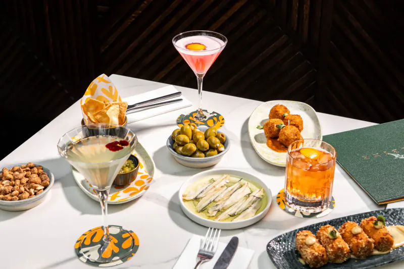 Elegant table with martini cocktails, olives, anchovies, croquettes, peanuts, and tortilla chips in upscale setting.