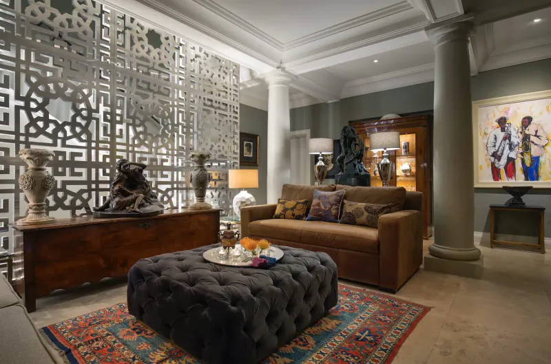 Elegant living room in 21 Nettleton, Clifton, Cape Town: brown sofa, black ottoman with drinks, ornate screens, sculptures, columns, African art.