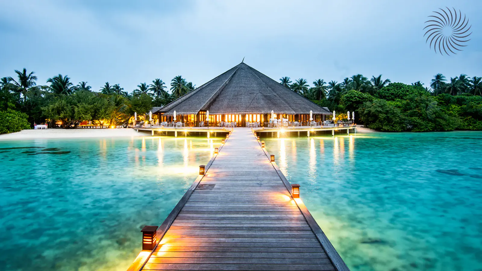 Hideaway Beach Resort & Spa: thatched roof bungalow on pier over glowing turquoise lagoon at dusk, palm trees.