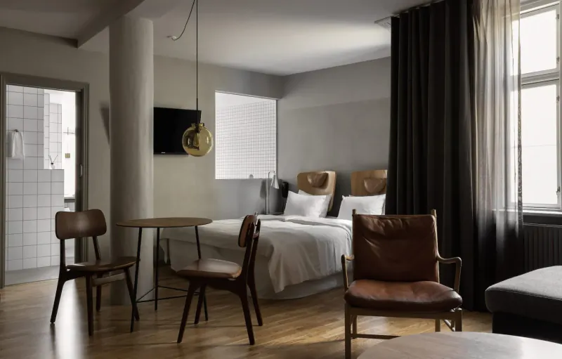 Modern Hotel SP34 room in Copenhagen with wooden bed, leather chairs, round table, and pendant lamp.