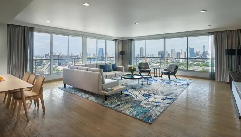 Spacious luxury hotel suite living room with white sofas, dining table, and panoramic city skyline views.