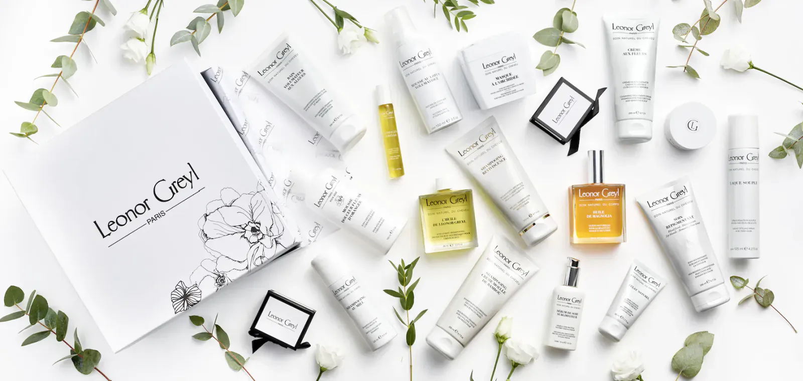 Leonor Greyl hair care products on white surface with eucalyptus leaves: open book, perfume, creams, serums.