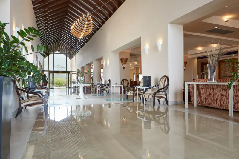Spacious hotel lobby in Giannoulis Cavo Spada Crete with wooden beamed ceiling, hanging light, chairs, plants, and polished floor.