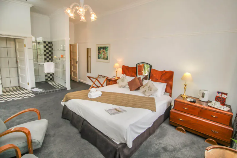 Elegant hotel room at Montagu Country Hotel with king bed, orange headboard, dresser, armchair, and en-suite shower.