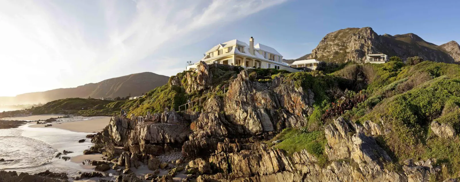Luxury white mansion perched on green cliffs overlooking sandy beach and ocean at sunset in Hermanus