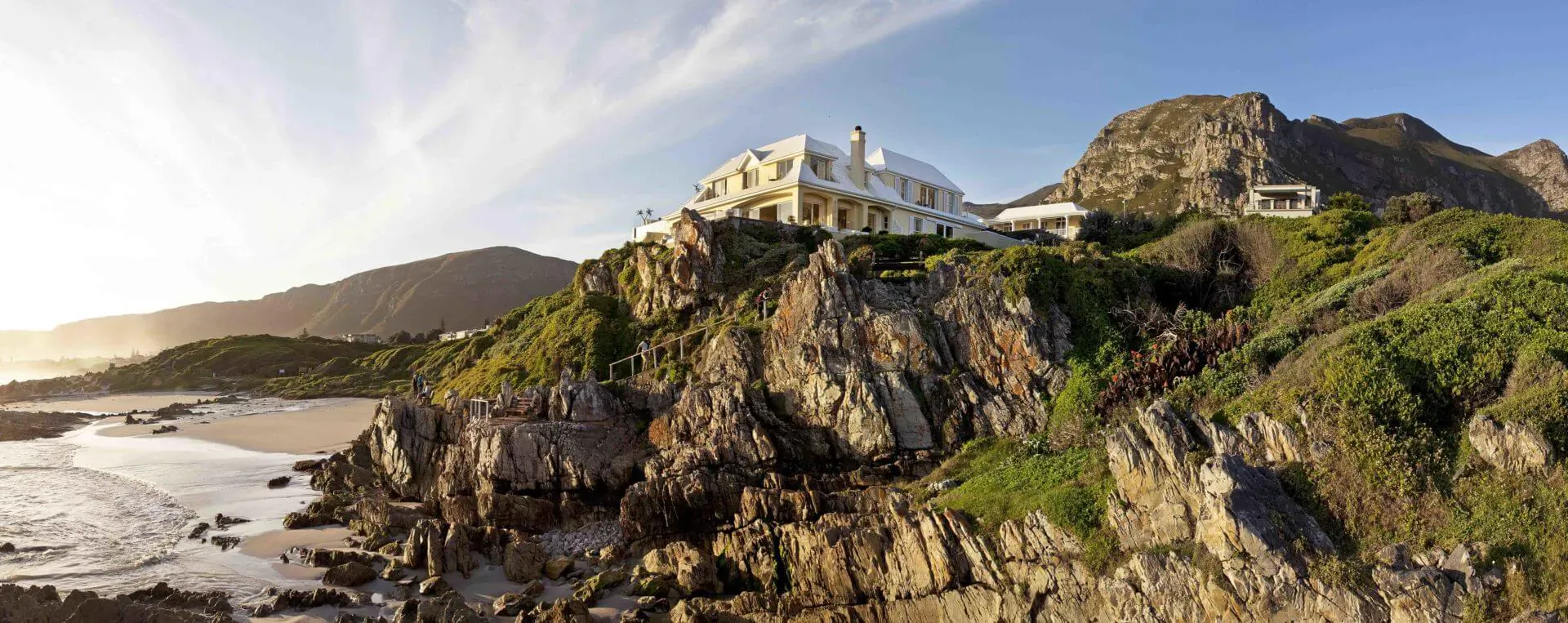 Luxury white mansion perched on green cliffs overlooking sandy beach and ocean at sunset in Hermanus