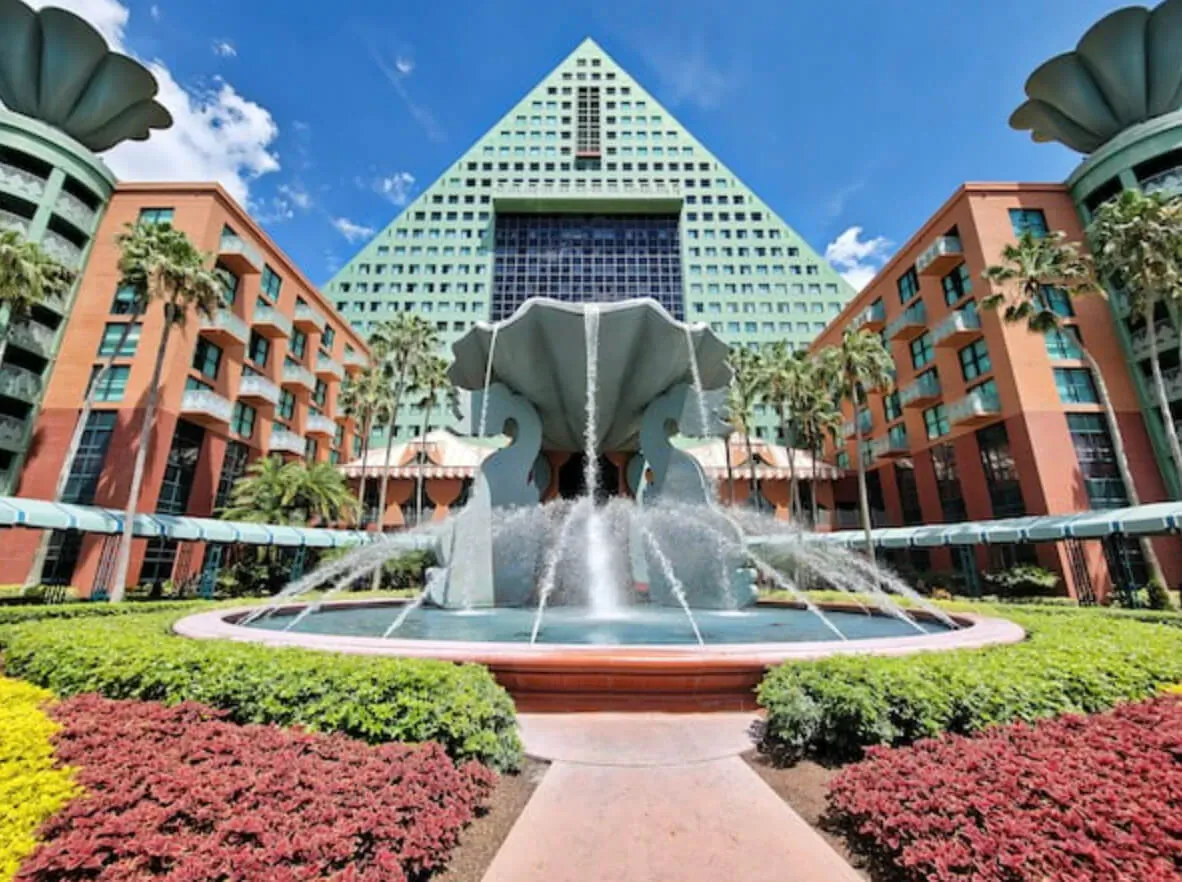 Pyramid-shaped hotel with teal towers, central fountain, palms, and gardens in sunny Orlando setting