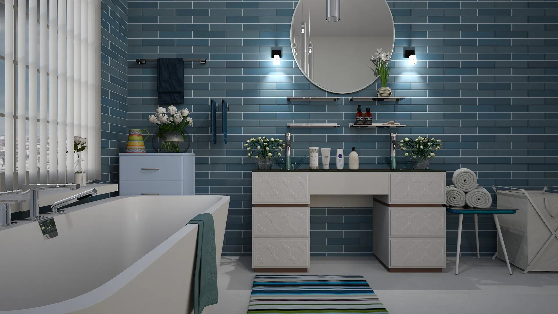 Modern blue-tiled bathroom with white vanity, round mirror, flowers, towels, and freestanding tub.