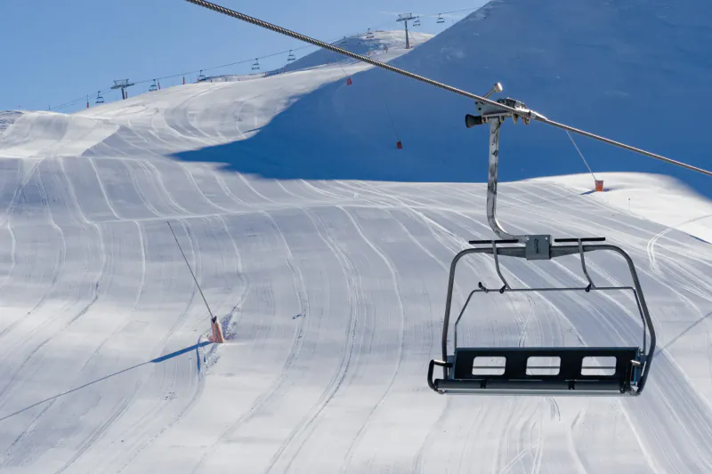 Empty ski lift chair ascending snowy slopes in sunny Pyrenees mountains with groomed runs and distant lifts.