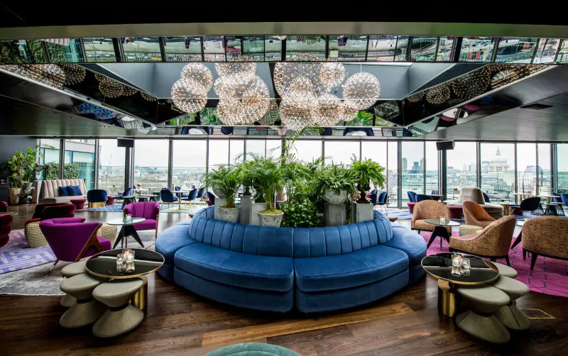 Luxurious rooftop lounge at Sea Containers London with blue circular sofa, orb lights, plants, and city skyline view.