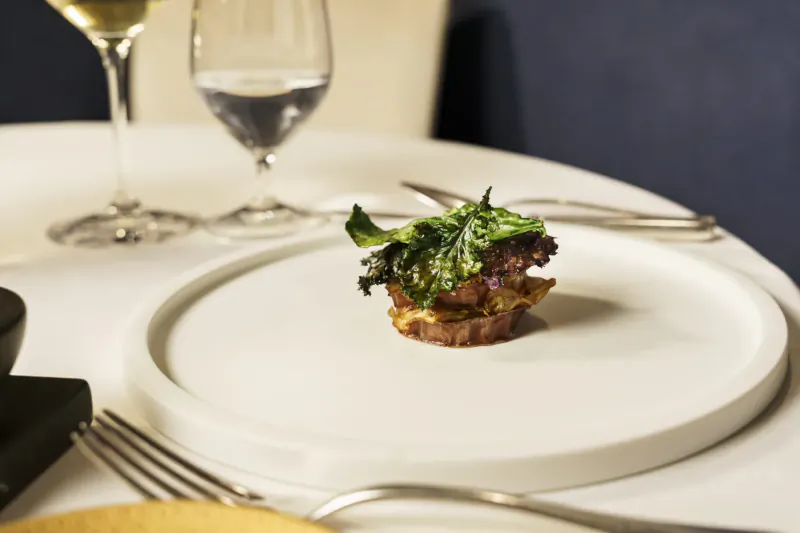 Close-up of stacked beetroot tart with green leaves on white plate, wine glass nearby on table