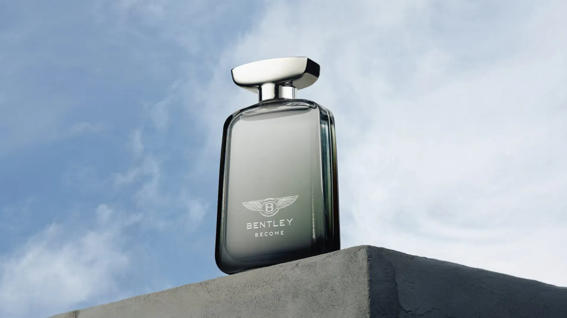Bentley Become men's fragrance bottle with silver cap on gray ledge against blue sky