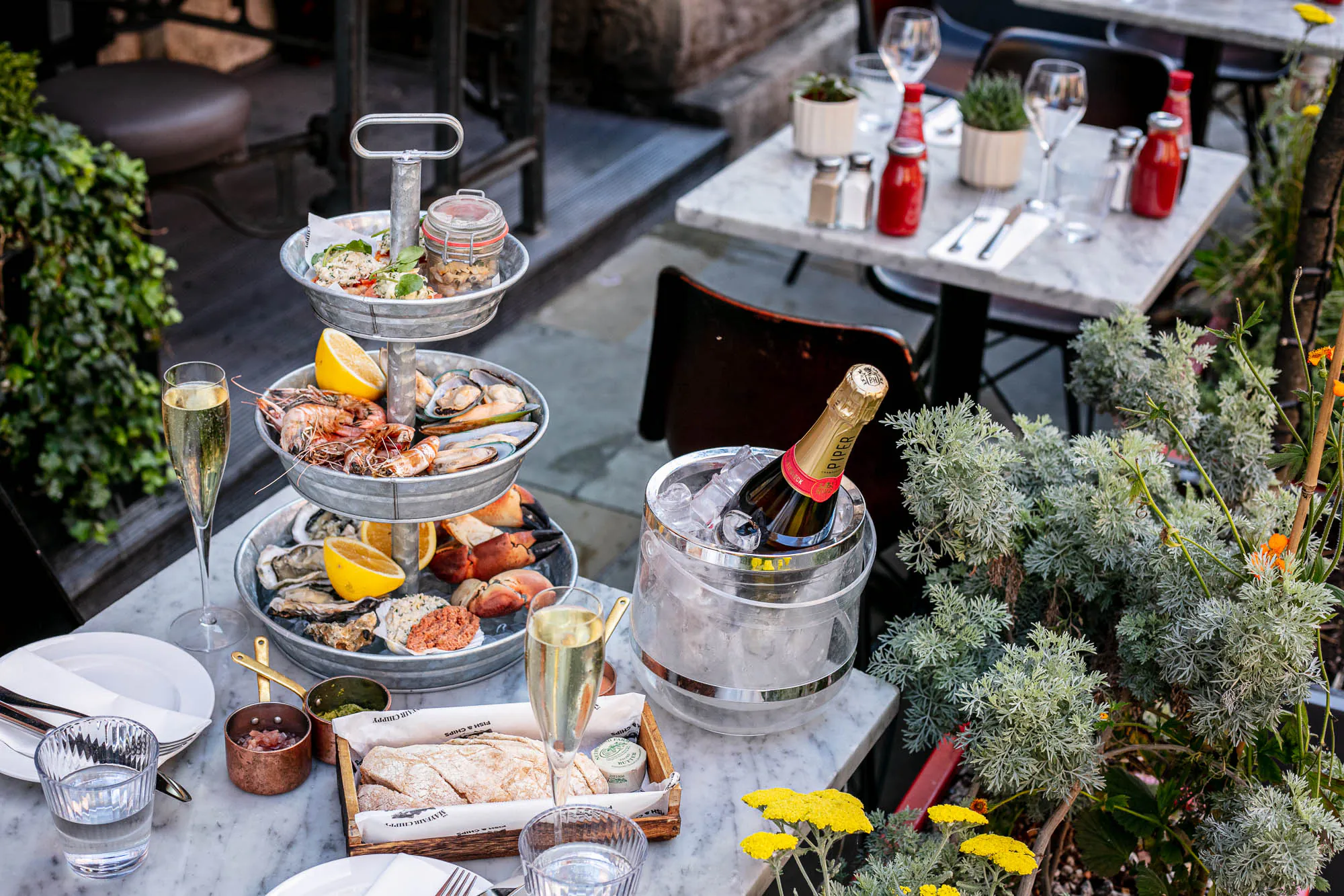 Tiered seafood platter with lobster, crab, oysters on outdoor table with champagne in ice bucket, glasses, at Lobster Pot Booth.