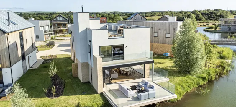Modern white luxury house with glass balcony overlooking lake and landscaped gardens at Silverlake Dorset