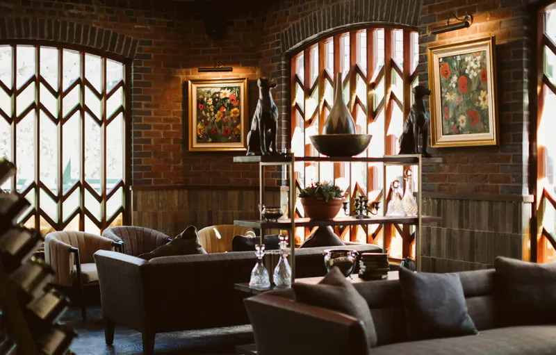 Cozy lounge in The Rabbit Hotel & Retreat with brick walls, arched windows, leather sofas, bar shelves, art, and plants.