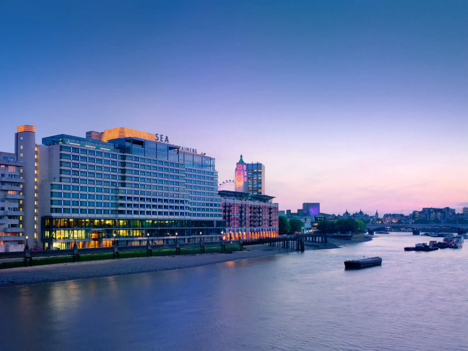 Sea Containers London hotel on the Thames riverbank at twilight, with lit towers and boats.