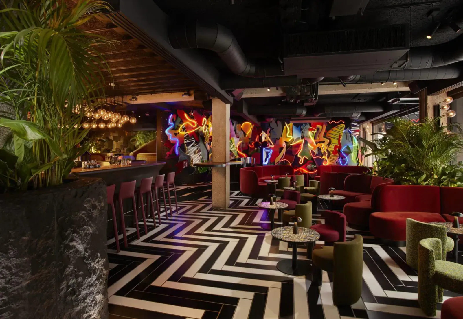 Vibrant Chotto Matte Soho bar with neon art wall, black zig-zag floor, red seating, plants, and event-ready lounge.