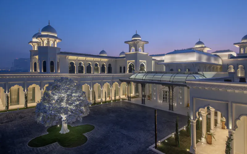 Twilight view of GHM luxury hotel courtyard in Qatar with white domed architecture, arches, and lit tree.