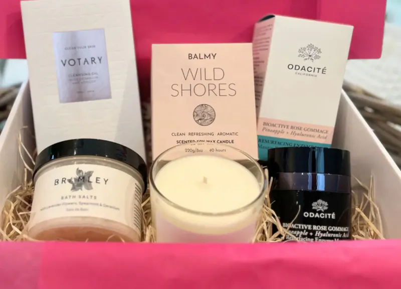 Pink luxury wellness gift box with Votary Wild Shores balm, Aesop bath salts, Diptyque candle, and Obagi cream.