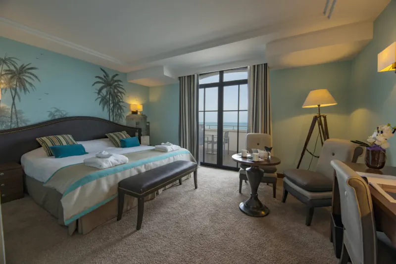 Luxurious sea-view hotel bedroom at Nouveau Monde Saint-Malo with king bed, bench, armchair, and balcony overlooking ocean.