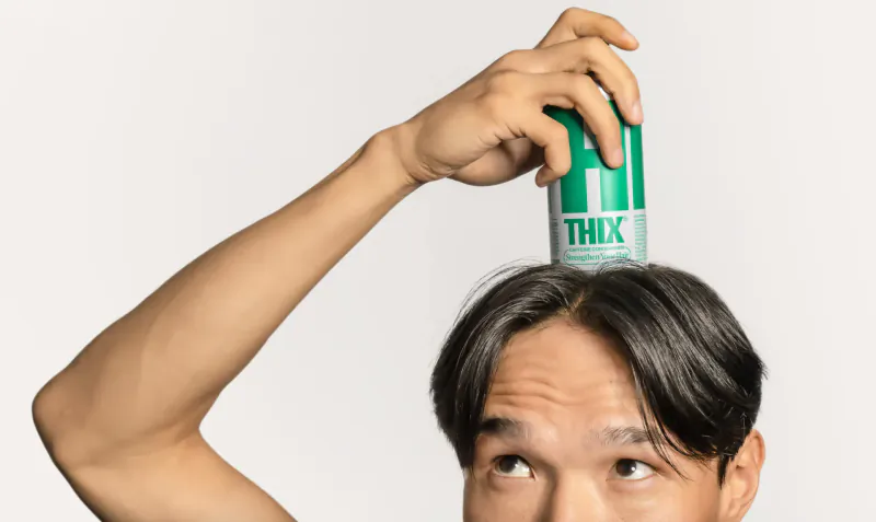Man balancing green THIX caffeine hair routine can on his head, smiling