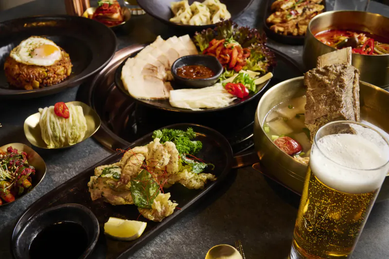 Assortment of Korean dishes including beef rib soup, fried seafood, rice with egg, and beer on table