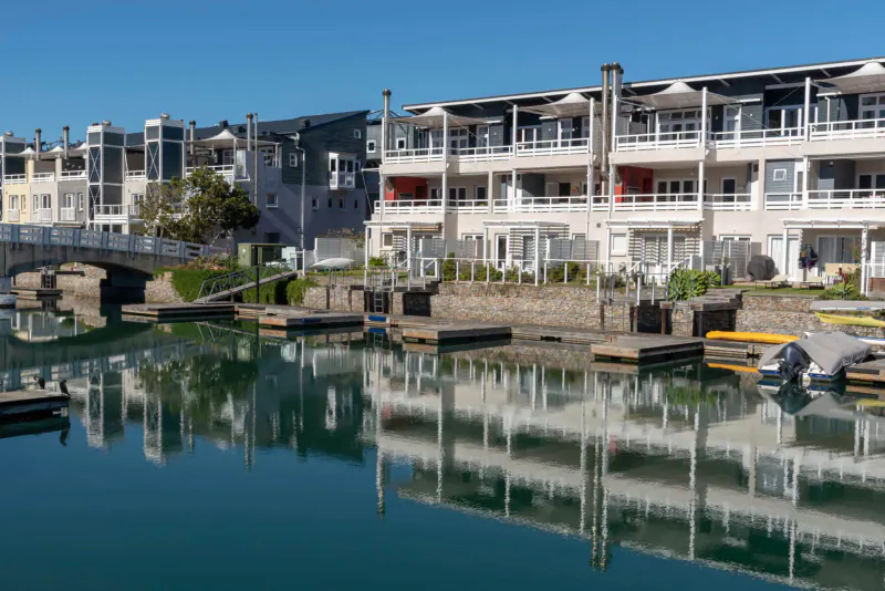 Luxury waterfront apartments at Turbine Boutique Hotel and Spa, with docks, boats, and reflections in calm water under blue sky.