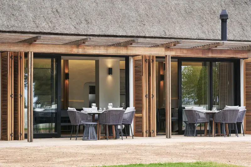 Clara’s Barn at Vergenoegd Löw: thatched roof veranda with open sliding doors to dining area with tables set on patio