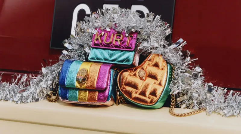 Kurt Geiger holiday bags on red 'GARB' sign with silver tinsel: rainbow stripe, heart, and puffy quilted designs.