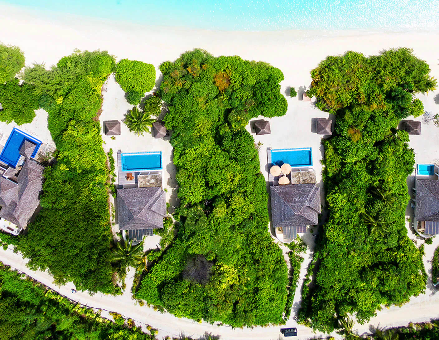 Aerial view of Hideaway Beach Resort & Spa in Maldives: thatched villas with blue pools nestled in lush greenery along white sandy beach and turquoise lagoon.