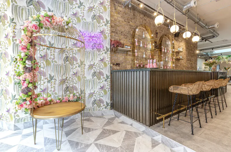 Floral pink Galentine’s arch beside wooden bar stools at Duck & Dry, patterned walls and pendant lights.
