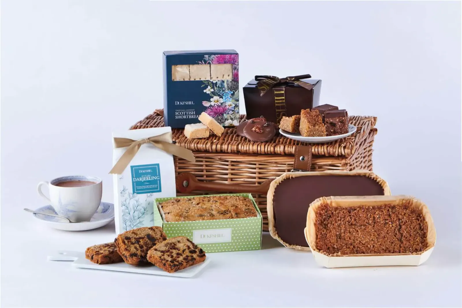 Wicker picnic basket overflowing with brownies, cookies, cakes, shortbread, and tea cup on saucer