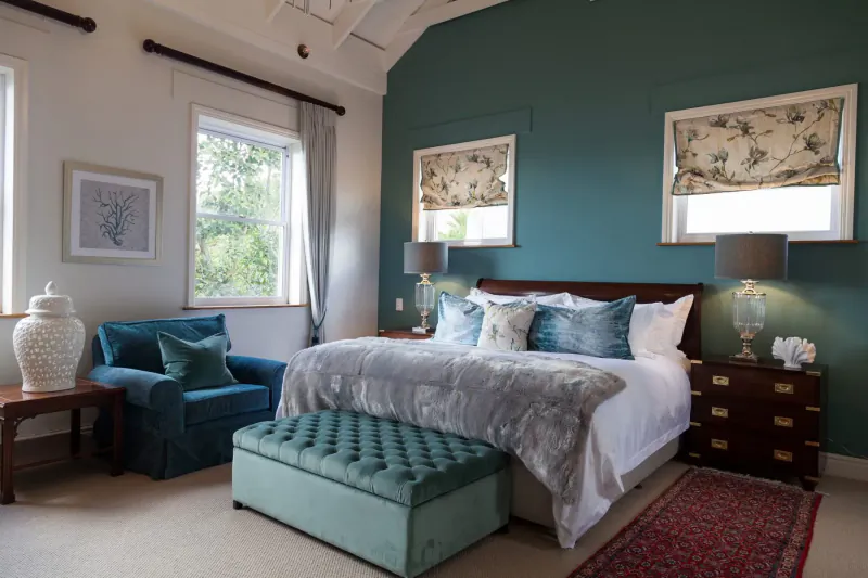 Luxurious bedroom at Tintswalo Boulders with teal walls, king bed with gray bedding, velvet armchair, and garden views.